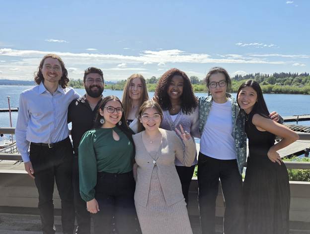 Photo taken at the Waterfront Activity Center, with Lake Washington in the background, of all clinical graduate students who presented at the research festival in 2026 (L to R) Connor Smith, Sam Lucero, Jess Meikle, Mikela Ritter, Yuqing Lei, Saivone Sanchious, Jinhan Zhu, and Christine Chang 