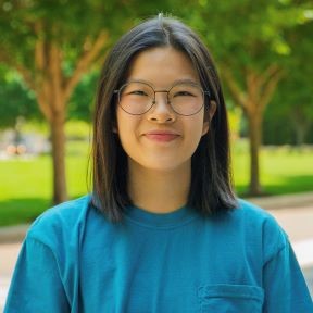 Headshot of Anna facing the camera, smiling, in a blue shirt with green background