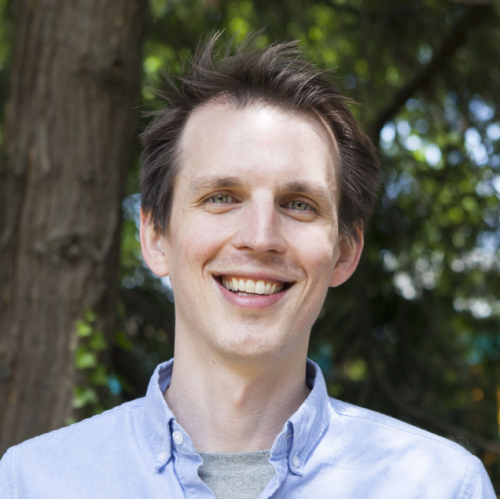 smiling headshot of Shawn in a blue shirt with a background of trees